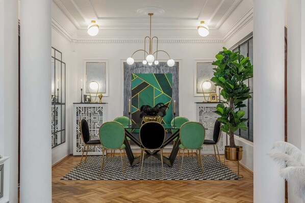 A dining area with a checkered floor, a central table with chairs, a chandelier, and a large green abstract painting on the wall. - Holt - The Great Gatsby (Bucharest)