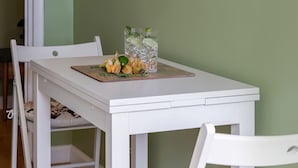 Un coin repas avec une table et des chaises blanches, une illustration botanique encadrée accrochée au mur, et un verre d’eau posé sur la table.