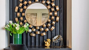 Un intérieur moderne avec un mur en lambris de bois foncé, un grand miroir rond doté d’un cadre doré, un fauteuil sombre et un vase vert orné de fleurs.