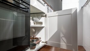Une cuisine équipée d’un four encastré, d’un meuble blanc contenant de la vaisselle et d’un sol carrelé.