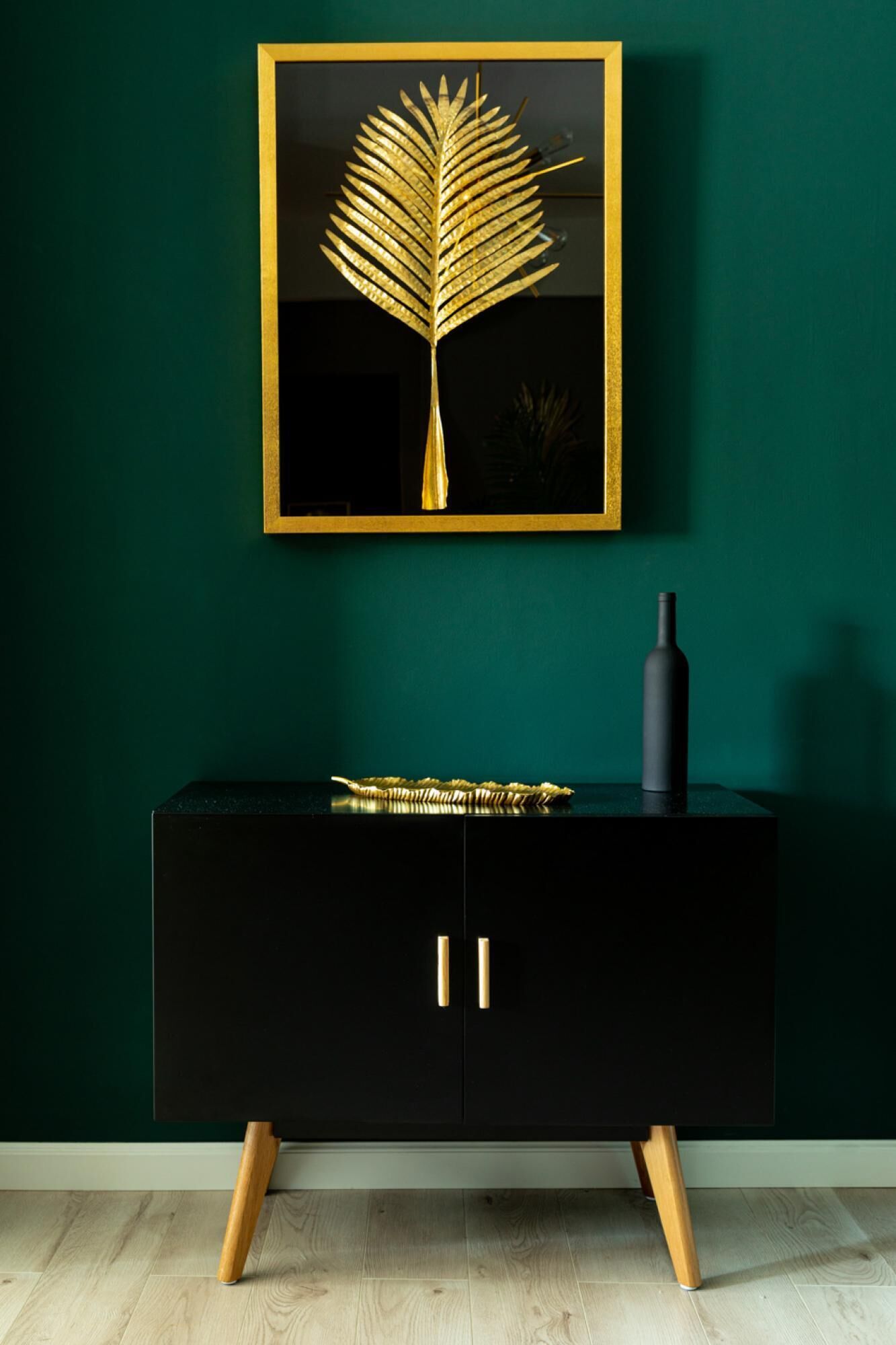 Un mobile nero con maniglie dorate, un'opera d'arte in foglia oro sopra e un vaso nero sopra il tutto.