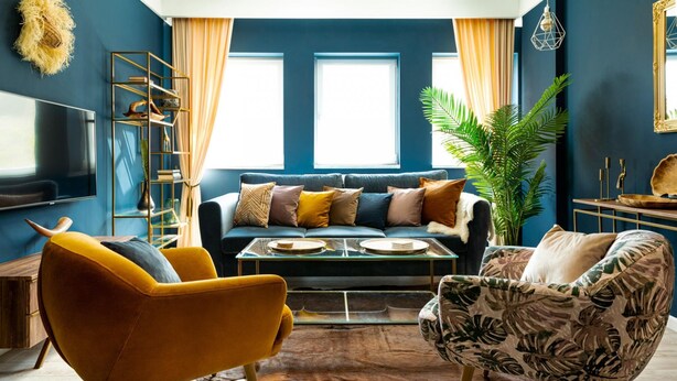 Uma sala de estar moderna com uma parede azul decorativa, um sofá, duas poltronas, uma mesa de centro e uma planta grande.