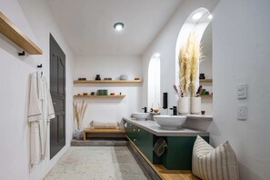 A modern bathroom with a large mirror, a white sink, and a vanity with a green cabinet. There are shelves above the sink holding decorative items and a towel rack on the left wall. - Sleeps 9 Outdoor Space Pingpong Table in Villa (Oaxaca)