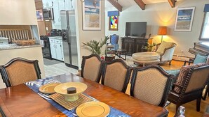 A dining area with a long wooden table set for four, surrounded by upholstered chairs.