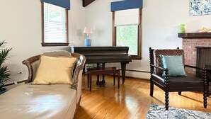 A living room with a piano, a sofa, a chair, and a fireplace.