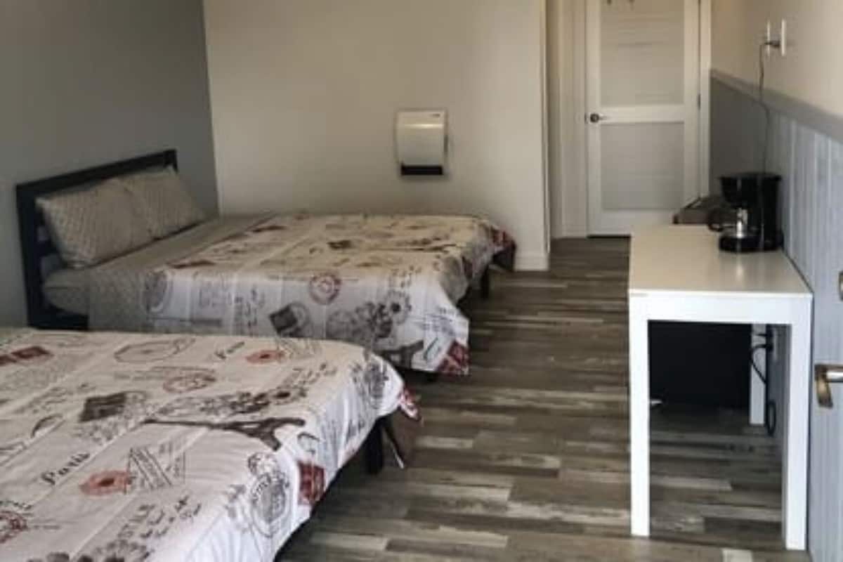 Une chambre d’hôtel avec deux lits simples, une petite table et une porte donnant sur une autre pièce.