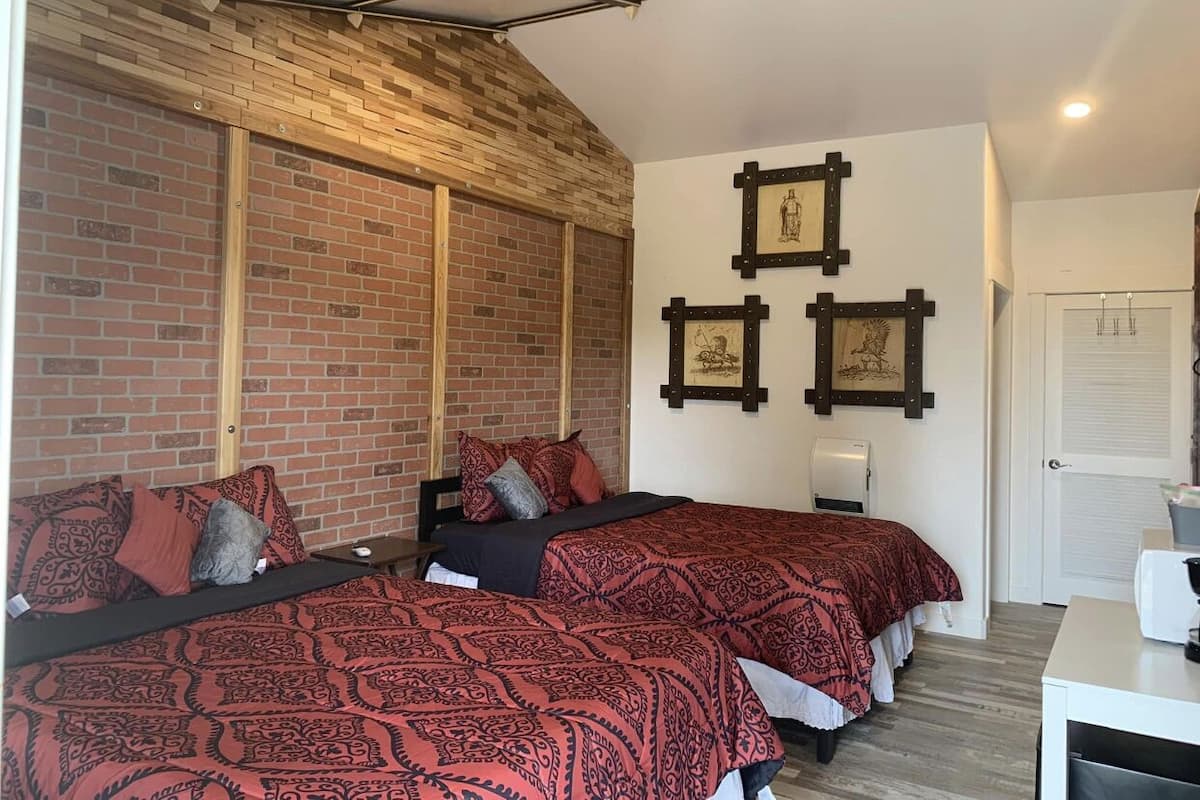 Une chambre avec deux lits, un mur en briques, des poutres en bois et des tableaux encadrés accrochés au mur.