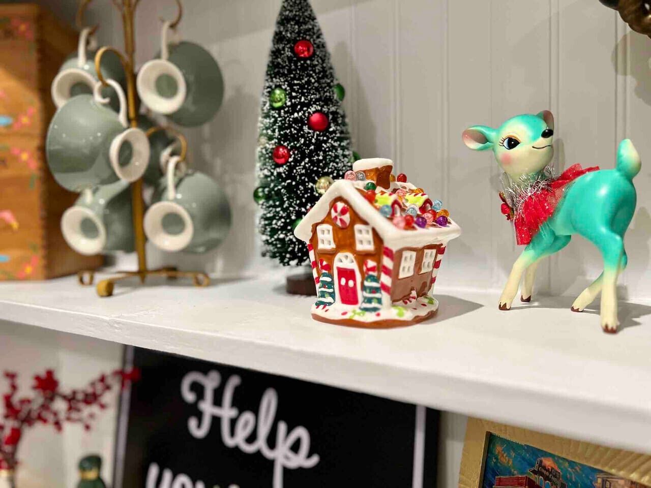 A shelf with a gingerbread house, a small Christmas tree, and a figurine of a dog.