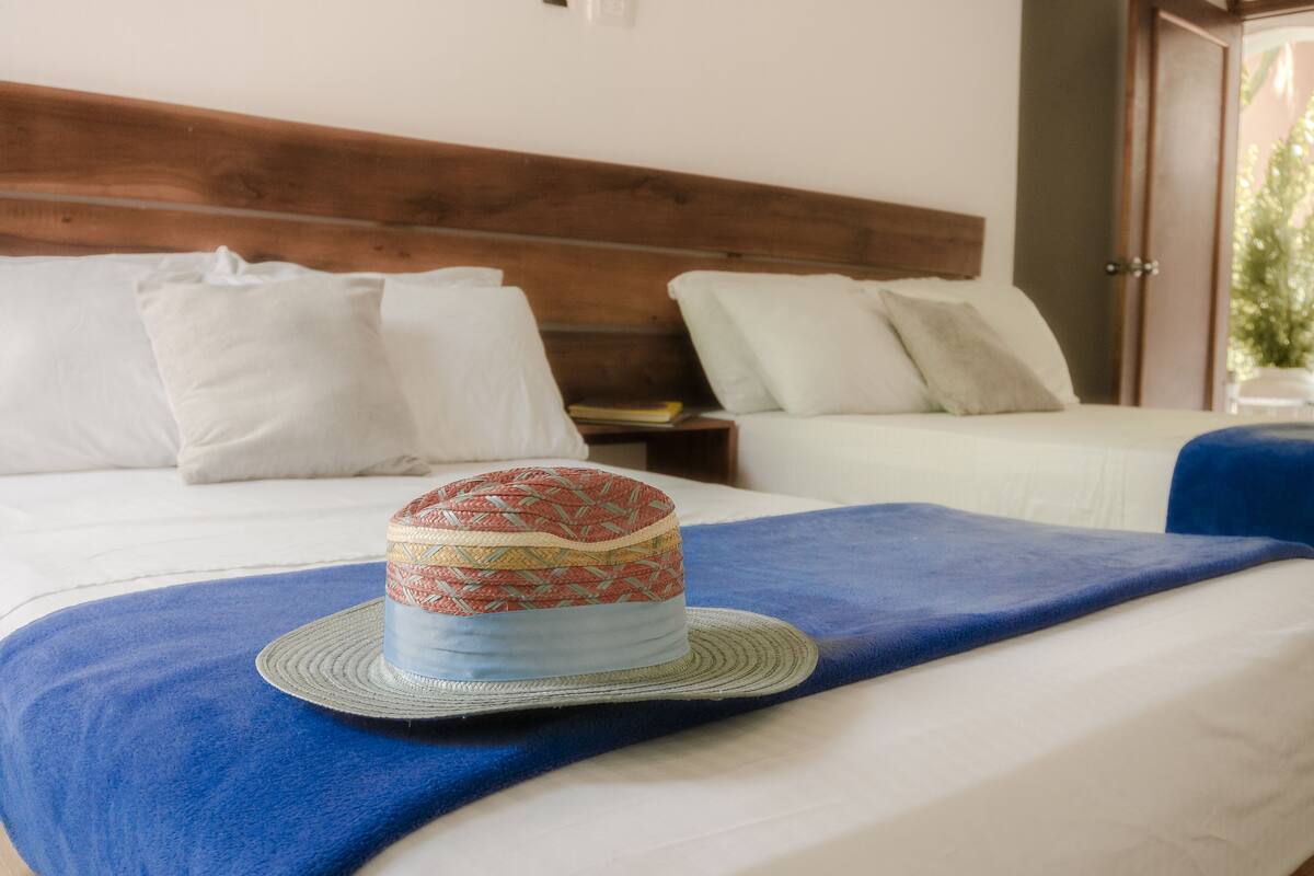 A hotel room with two beds, a wooden headboard, and a blue throw blanket.