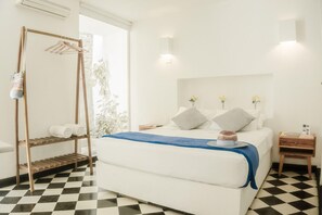 Ein Schlafzimmer mit Schachbrettfußboden, einem Bett mit blauer Decke, einem Wäscheständer aus Holz und einem Nachttisch mit Lampe.