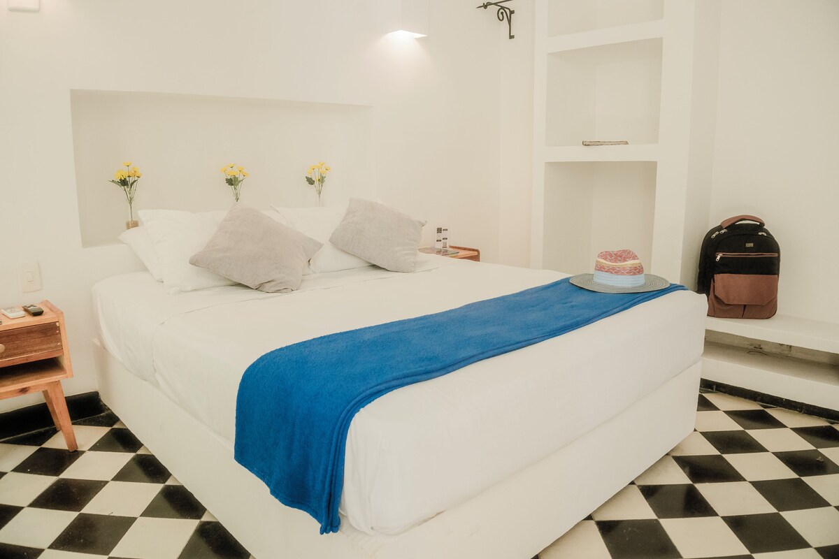 A hotel room with a bed, a nightstand, a suitcase, and a checkered floor.