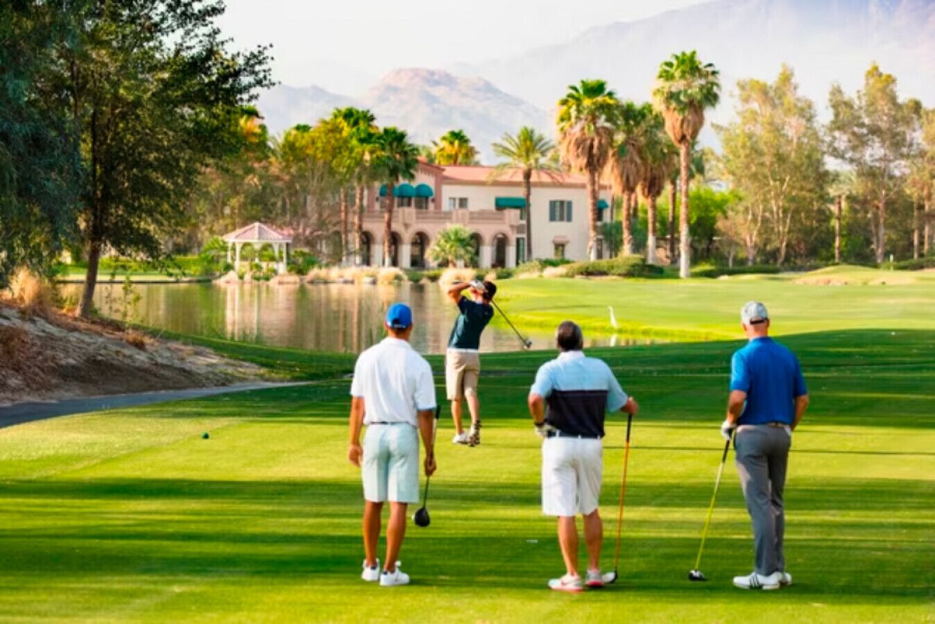 A golf course with a pond, palm trees, and a building in the background.