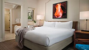 Une chambre d’hôtel avec un grand lit, une table de chevet, une lampe, un tableau encadré au mur et une vue sur la salle de bain.