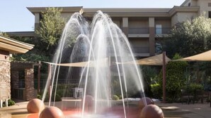 Una fuente con chorros de agua en un patio con un edificio al fondo.