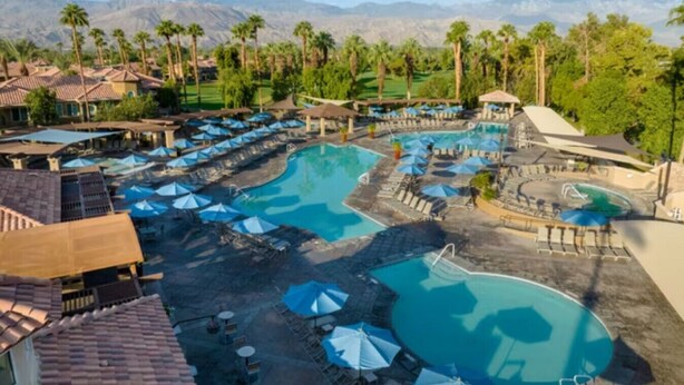 Un resort con varias piscinas, zonas de descanso y palmeras.