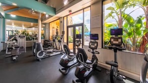 A gym with various exercise equipment, large windows with a view of greenery, and a ceiling with wooden beams.