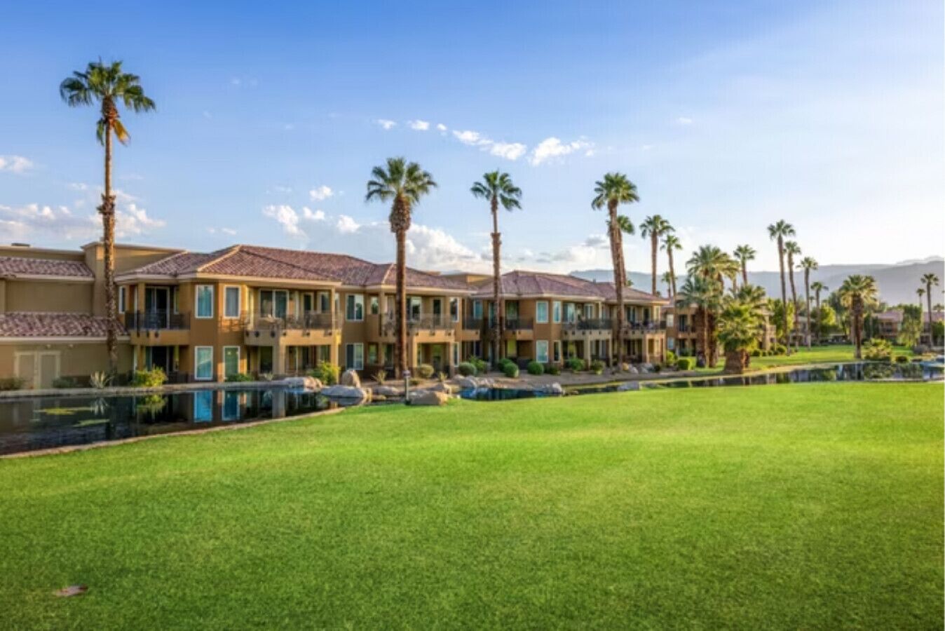 Een meerhoog hotel met een zwembad, palmbomen en een heldere lucht.