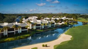Un campo da golf con un elemento d'acqua, un'area sabbiosa e moderni edifici dotati di piscina.