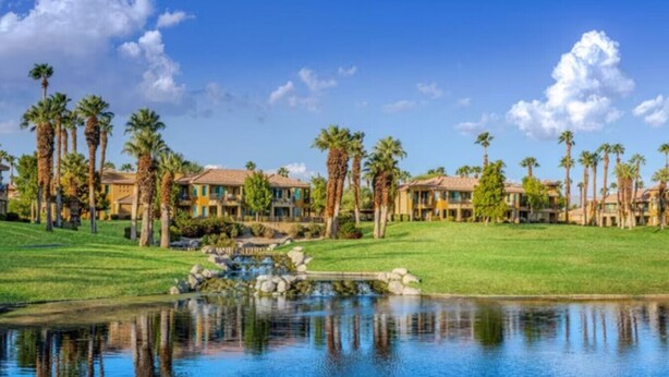 A golf course with a pond, palm trees, and a row of houses.