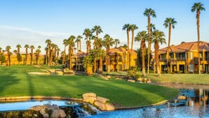 A golf course with a water feature, palm trees, and a building with a red roof.