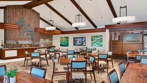 A spacious dining area with wooden tables and chairs, a kitchen in the background, and a wall with a 'ZIMMIE'S' sign. - Sheraton Vistana Resort (1BR) (Orlando)