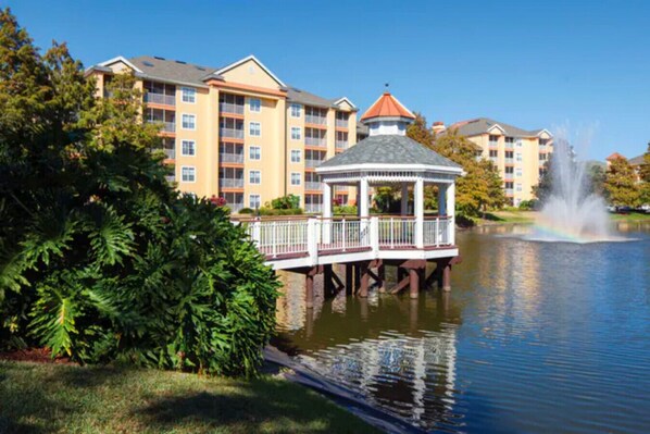 Un hotel con un pabellón sobre un lago, rodeado de follaje y una fuente.