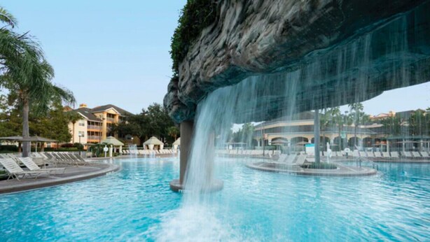 A swimming pool with a waterfall feature, lounge chairs, and a building in the background. - Sheraton Vistana Resort (1BR) (Orlando)