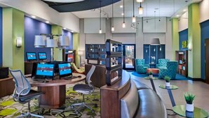 A modern lobby with a reception desk, multiple computer monitors, seating areas, and a large bookshelf.