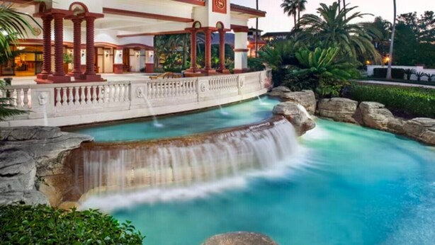 A pool with a waterfall feature, surrounded by rocks and greenery.