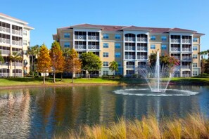 A multi-story hotel with balconies, a pond with a fountain, and surrounding greenery. - Sheraton Vistana Villages (2BR) (Orlando)