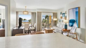 Habitació d'hotel amb zona de menjador, sofà, televisió i una finestra gran amb vista a l'oceà.