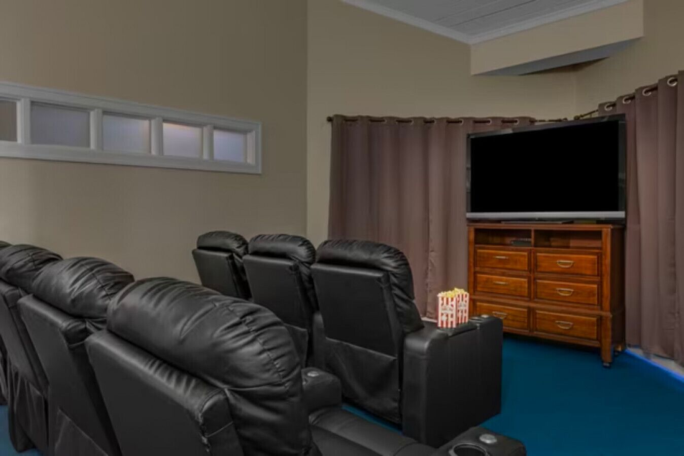 Una sala de cinema amb butaques de cuir reclinables, un televisor de pantalla plana gran i un moble de roba de fusta.