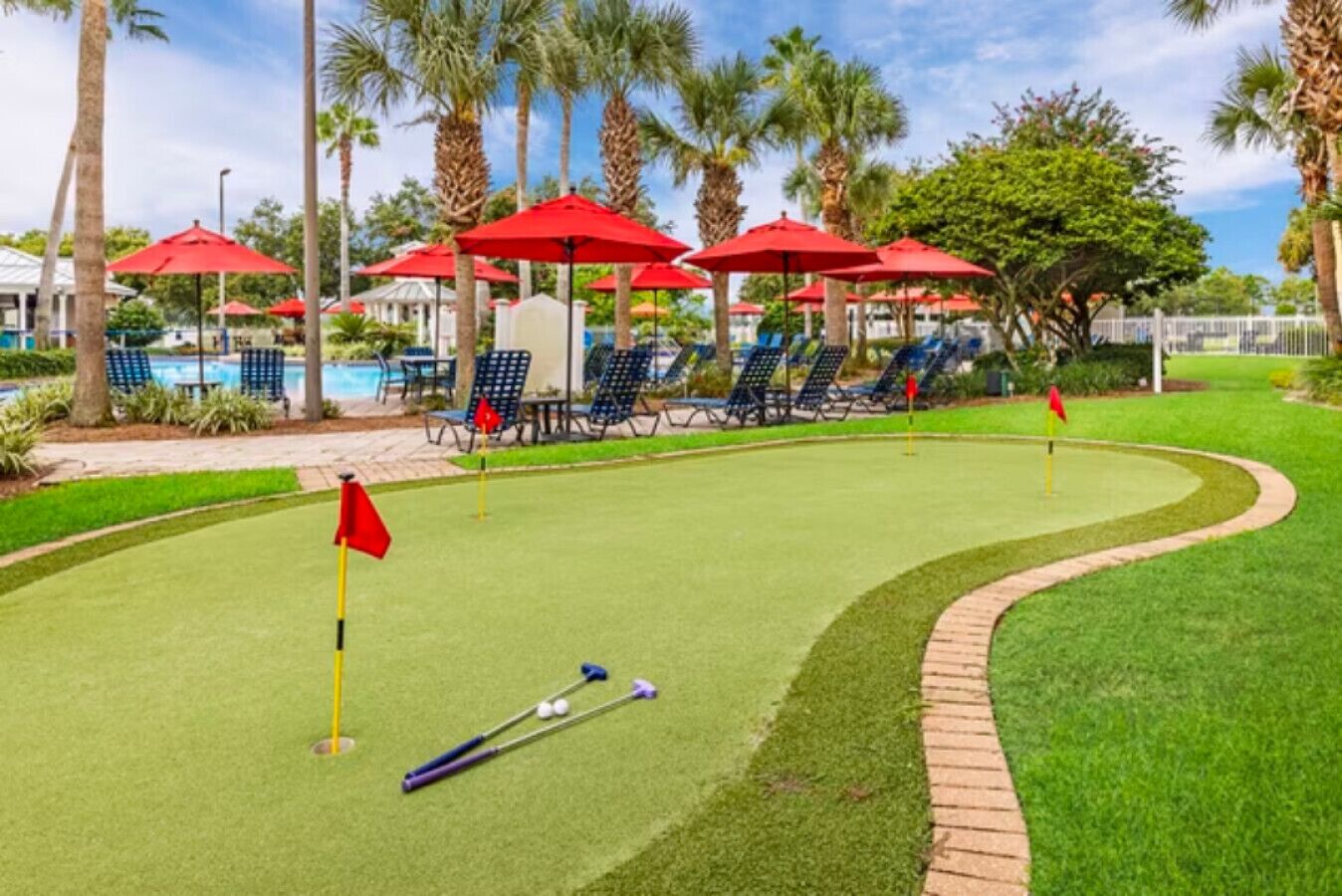 Ein Minigolfplatz mit roten Fahnen, einem Putting-Green und Liegestühlen im Hintergrund.