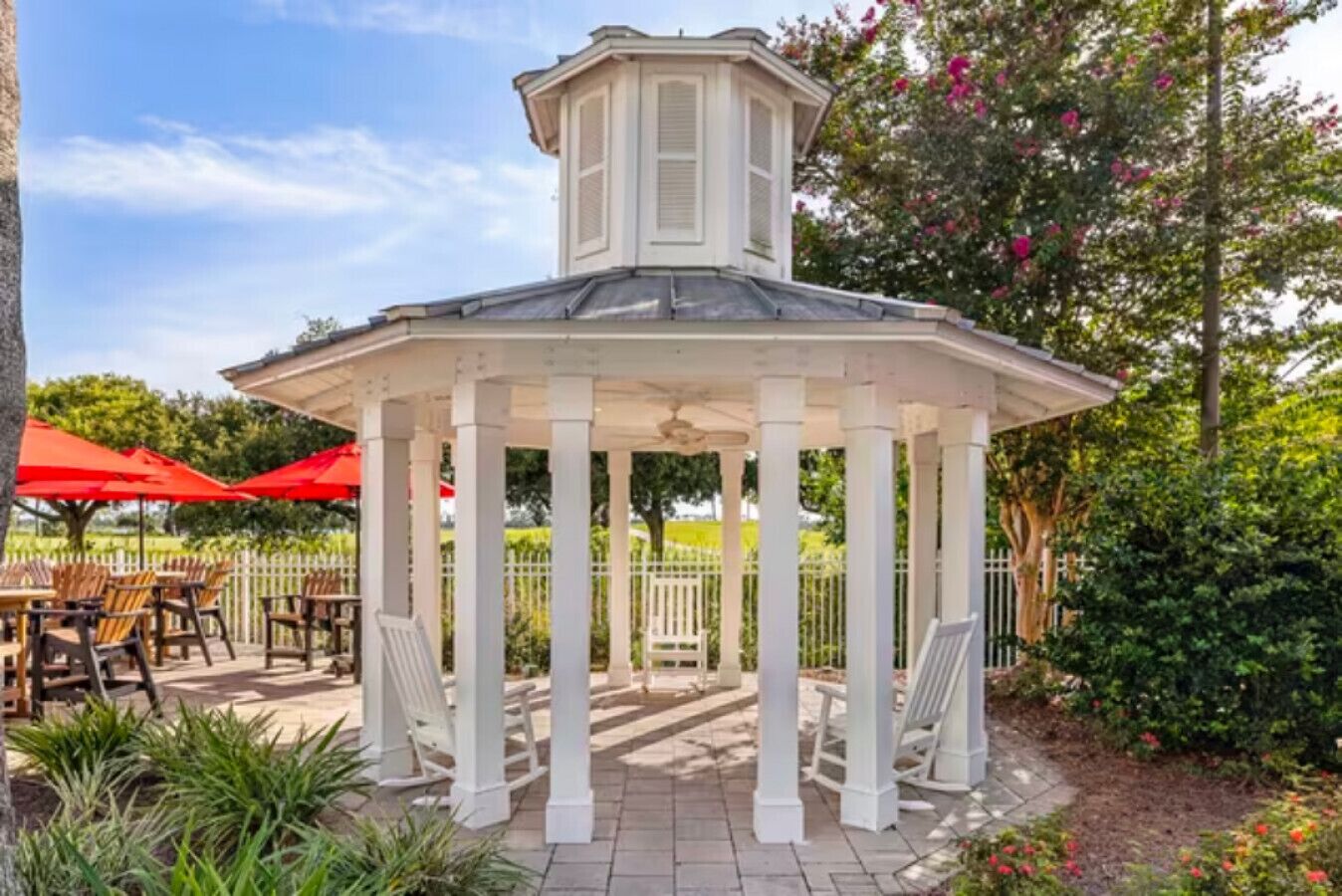 A gazebo with white columns and a peaked roof, surrounded by outdoor seating and greenery.
