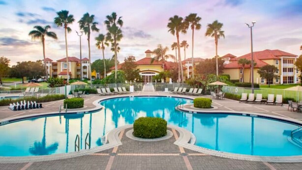 A large swimming pool with a curved design, surrounded by lounge chairs and palm trees. - Sheraton PGA Vacation Resort (2BR) (Port St. Lucie)