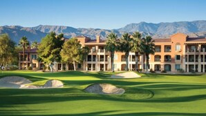 Un terrain de golf avec, en arrière-plan, un ensemble de bâtiments comprenant plusieurs étages, le tout surplombé par un paysage montagneux.