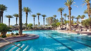 Une piscine à l’eau d’un bleu cristallin, entourée de palmiers et agrémentée d’espaces ombragés avec des parasols.