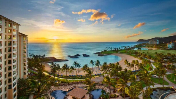 Ein Resort mit Pool, Palmen und Blick auf den Ozean im Sonnenuntergang.