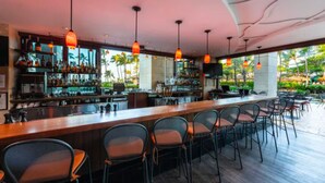 Eine Bar mit einer langen Theke, mehreren Stühlen und hängenden Pendelleuchten.