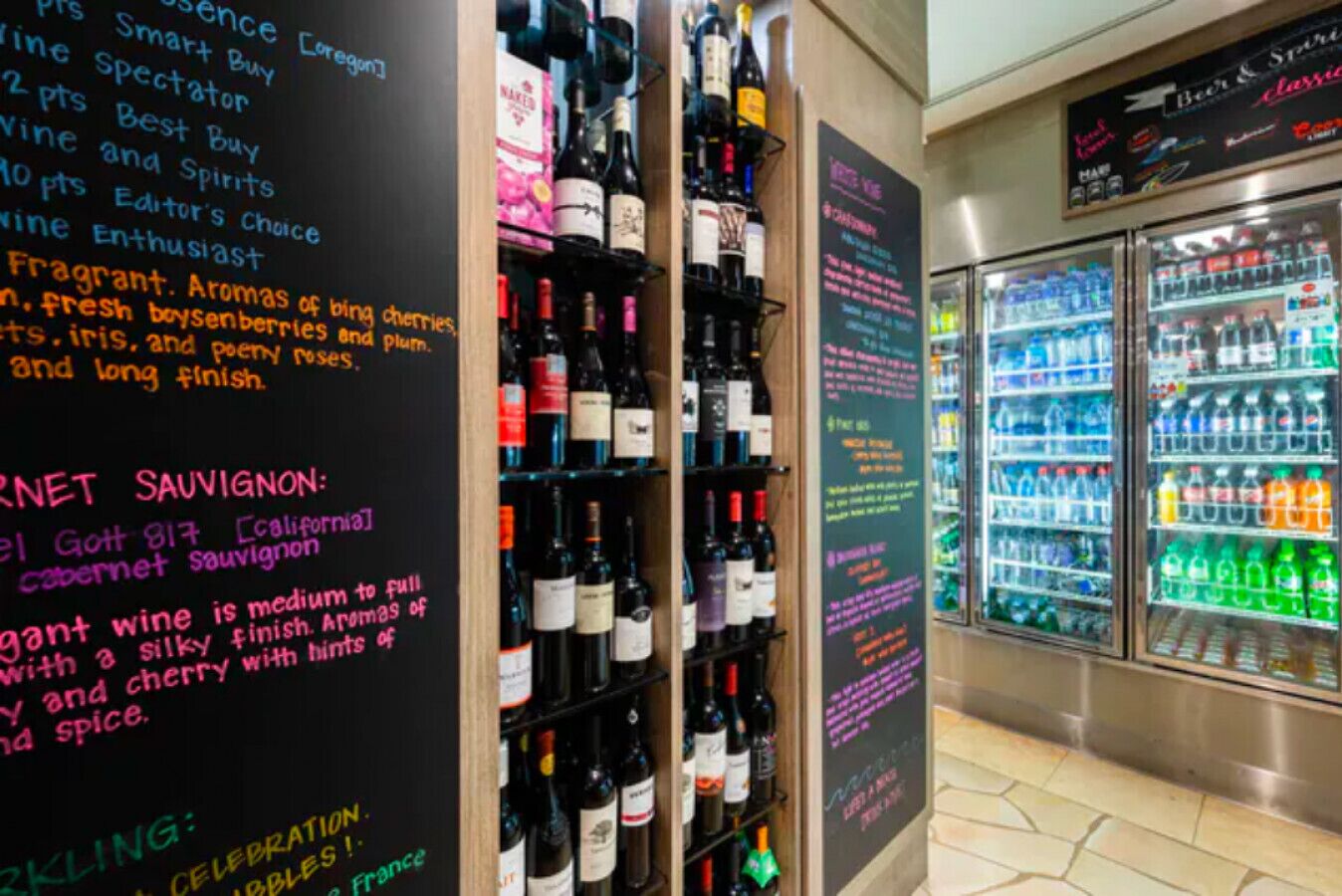 Una tienda de vinos con estantes llenos de botellas variadas y una pizarra con el menú que detalla tipos de vino y precios.