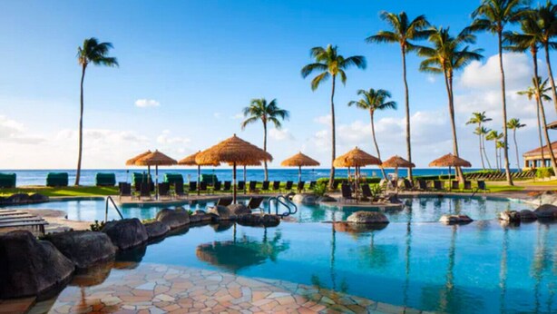 A pool area with lounge chairs and umbrellas, surrounded by palm trees and a view of the ocean. - Sheraton Kaua‘i Resort Villas (2BR) (Koloa)