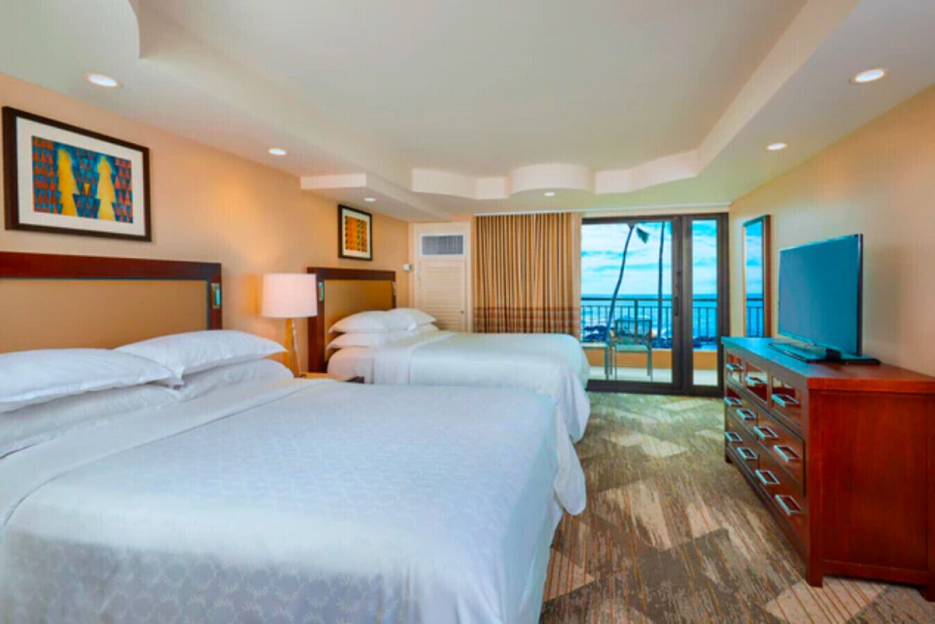 Habitación de hotel con dos camas, televisión, cómoda y balcón con vistas.