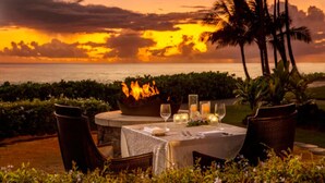 A table set for dining with a fire feature, surrounded by chairs, and overlooking a sunset over the ocean. - Sheraton Kaua‘i Resort Villas (1BR) (Koloa)