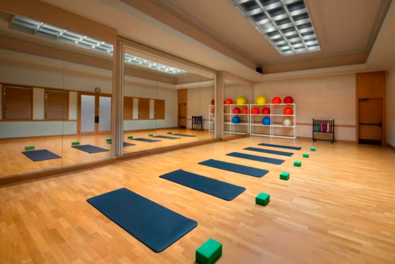 A spacious room with wooden flooring, large mirrors, and exercise mats arranged for physical activities.