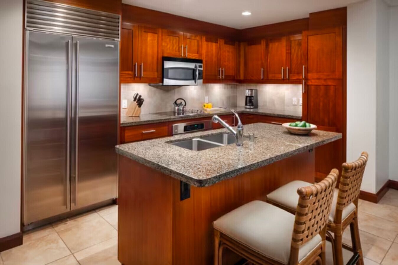 A modern kitchen with wooden cabinets, stainless steel appliances, a granite countertop, and a built-in island with bar stools.