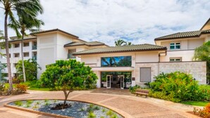 Entrada de hotel con jardín ajardinado, palmeras y cielo despejado.