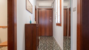 Un pasillo con una puerta de madera, un mueble pequeño y un espejo en la pared.