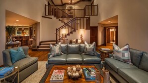 Un vaste espace de vie agrémenté d’un escalier moderne, de canapés en cuir et d’une table basse sur laquelle sont disposés des livres et des objets décoratifs.