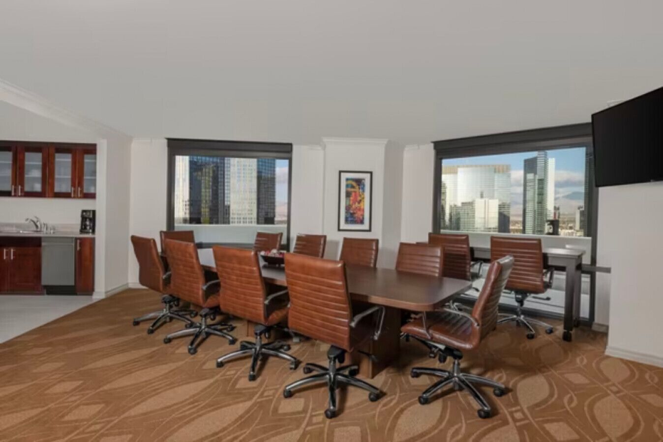 Une salle de conférence dotée d’une grande table et de chaises, d’un coin cuisine et de grandes fenêtres offrant une vue sur la ville.