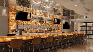 A bar area with a marble-like countertop, multiple bar stools, and a variety of bottles and glasses. - Marriott's Grand Chateau (Studio) (Las Vegas)